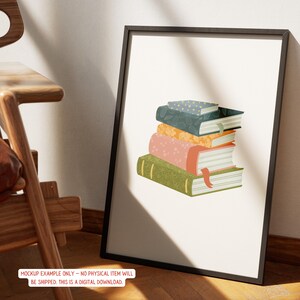 May include: A framed art print featuring a stack of illustrated books. The books are in various colors, including green, pink, orange, and blue, with decorative patterns and bookmarks. The frame is black, and the print is displayed against a neutral background.