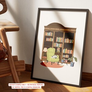 May include: A framed art print depicts a cozy reading nook. The illustration features a large bookshelf filled with colorful books, a green armchair with a cat, a small table, and a lamp. The artwork is in a black frame.