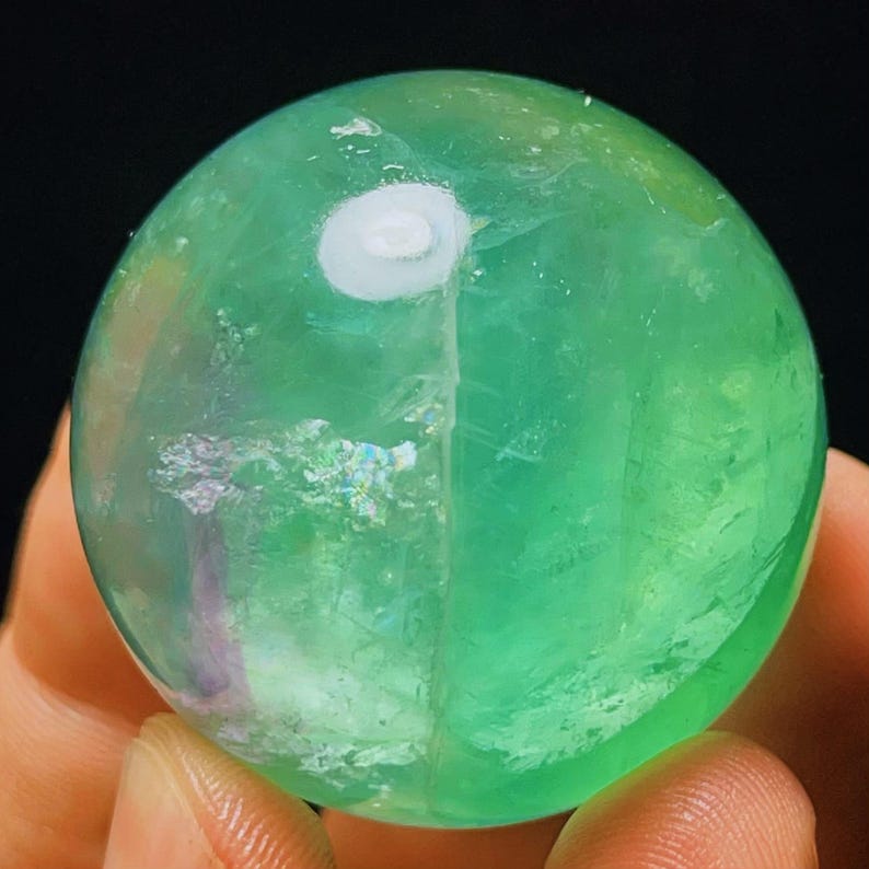 May include: A green fluorite sphere with iridescent inclusions. The sphere is polished and has a smooth surface.