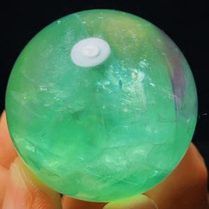 May include: A green fluorite sphere with a white centre. The sphere is polished and has a translucent appearance.