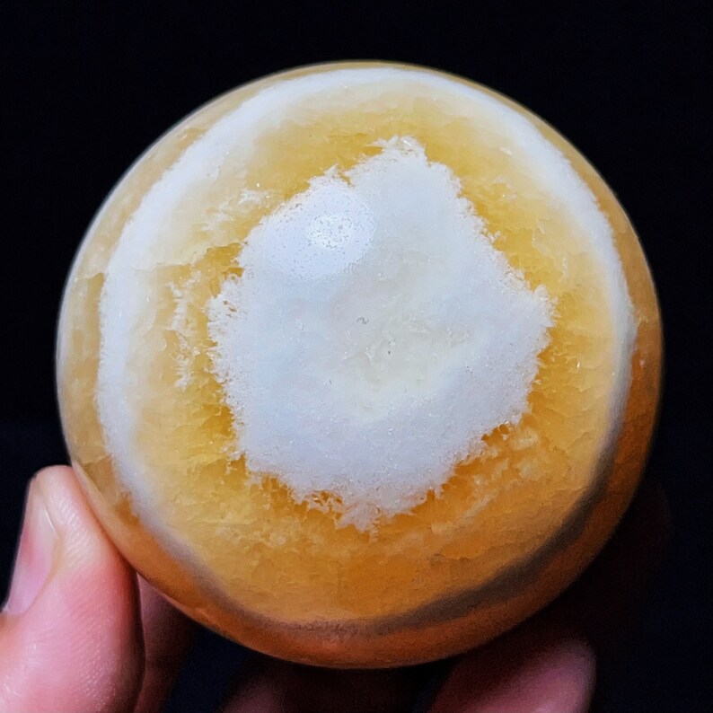 May include: A polished orange and white agate sphere with a swirling pattern. The sphere is smooth and has a glossy finish.