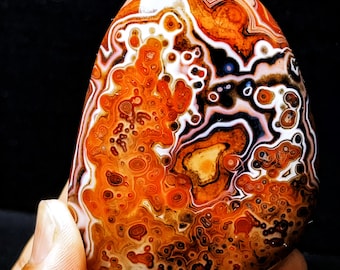 May include: A polished agate stone with a swirling pattern of orange, red, white, and black. The stone has a smooth, rounded surface.