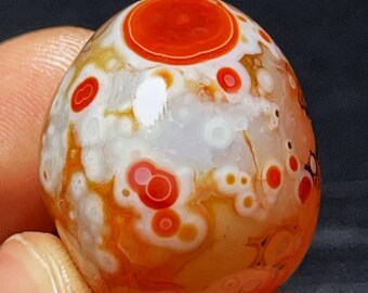 May include: A polished agate sphere with a white base and red, orange, and brown markings. The sphere has a unique pattern of concentric circles and dots.