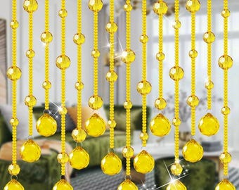May include: A curtain made of strands of gold beads. The beads are round and have a shiny finish. The curtain is hanging in front of a window.