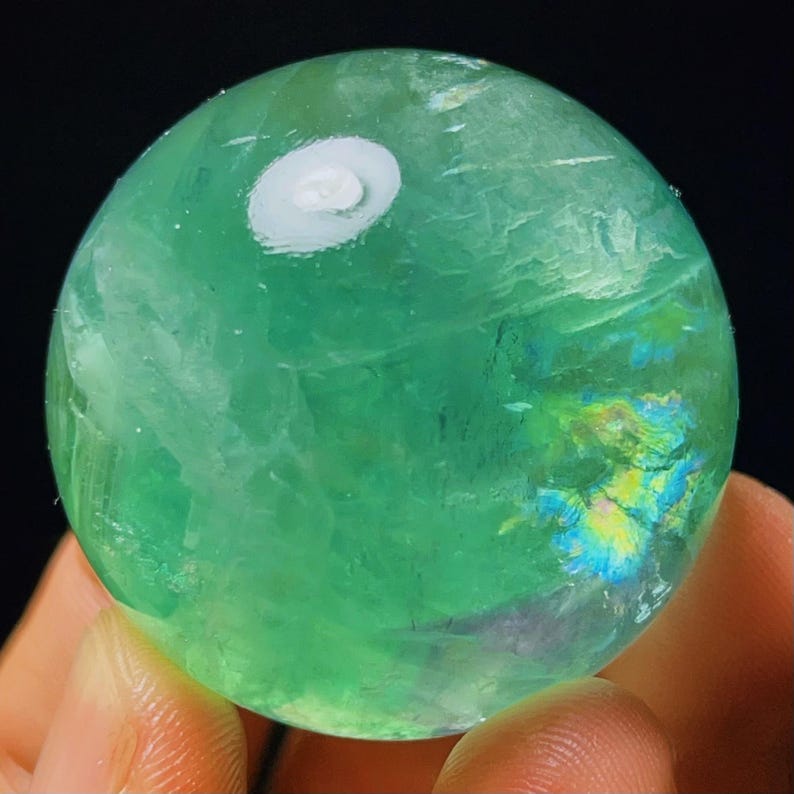 May include: A green fluorite sphere with iridescent inclusions. The sphere is polished and has a smooth surface.
