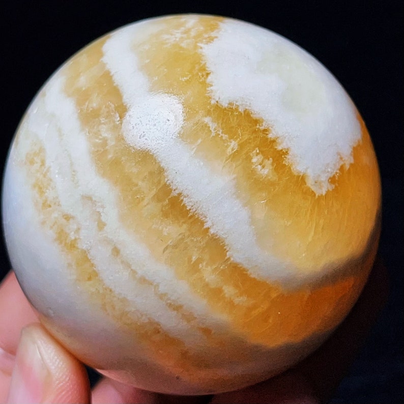 May include: A large, polished, yellow and white calcite sphere. The sphere has a swirling pattern of white and yellow bands.
