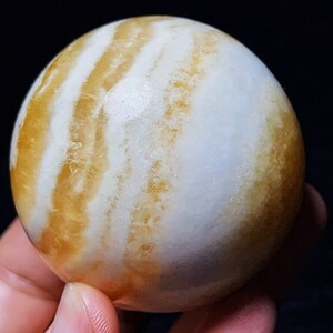 May include: A large, round, white and yellow agate sphere with a swirling pattern. The sphere is smooth and polished.