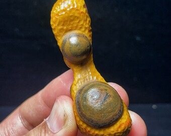 May include: A yellow and brown agate stone with a unique, peanut-shaped form. The stone has two circular, concentric patterns on its surface.
