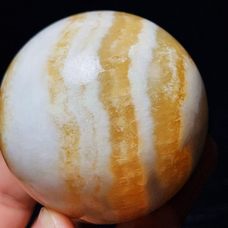 May include: A white and yellow striped sphere made of polished agate. The sphere has a smooth, glossy finish and is a natural stone.