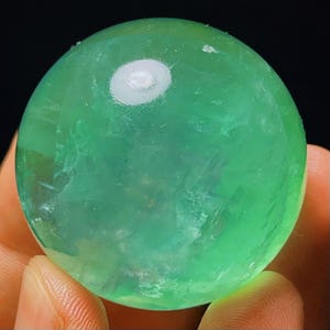 May include: A smooth, green fluorite sphere with a white, cloudy centre. The sphere is polished and has a translucent appearance.