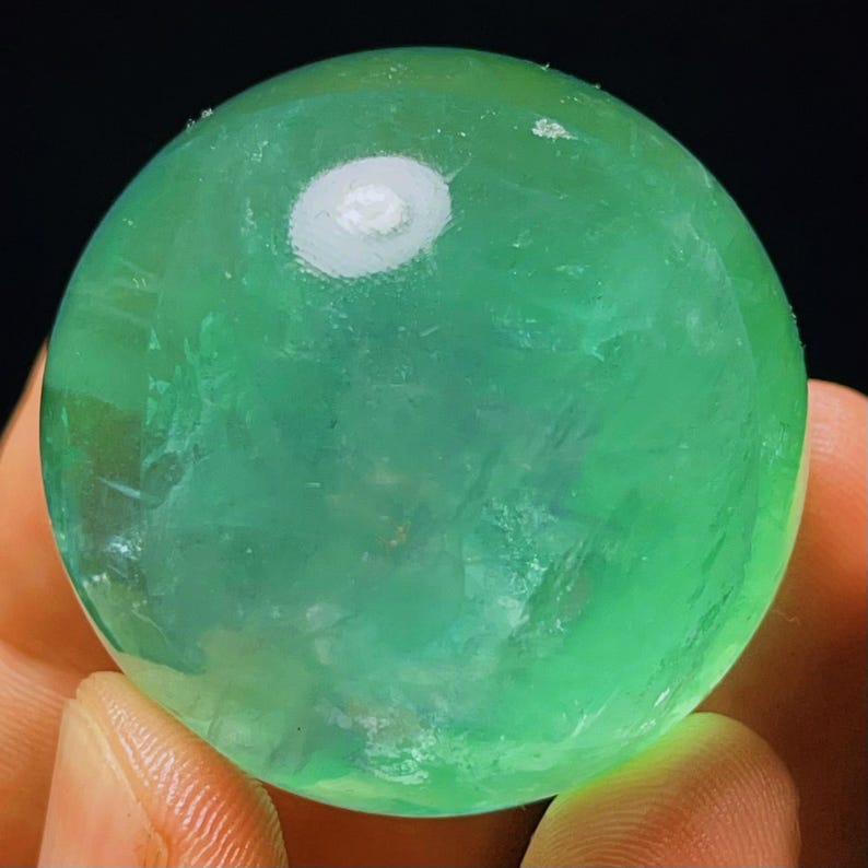 May include: A smooth, green fluorite sphere with a white, cloudy centre. The sphere is polished and has a translucent appearance.