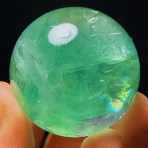 May include: A green fluorite sphere with iridescent patterns and a white swirl on the surface.