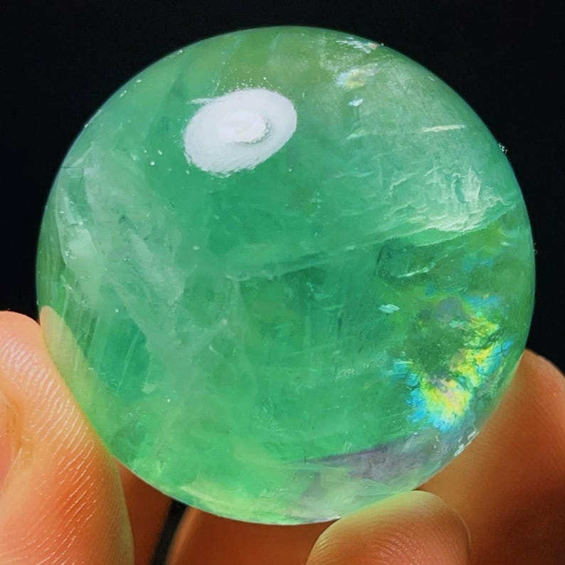 May include: A green fluorite sphere with iridescent patterns and a white swirl on the surface.