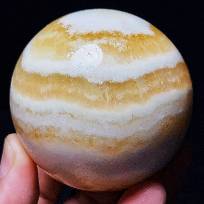 May include: A large, round, banded agate sphere with alternating layers of white and yellow-orange. The sphere is polished and smooth.