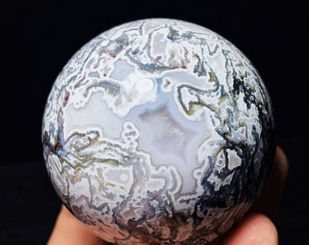 May include: A white, gray, and green agate sphere with intricate patterns and swirls. The sphere is smooth and polished.