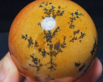 May include: A polished, orange agate sphere with black dendritic patterns. The sphere has a smooth, glossy finish and is approximately 2 inches in diameter.