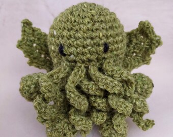 May include: Green crocheted plush toy shaped like Cthulhu, a fictional tentacled monster from the works of H.P. Lovecraft. The toy has black eyes and a friendly expression.