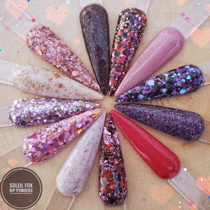 May include: A collection of nail dip powder samples in various colors and textures. The samples include glitter, shimmer, and solid colors, ranging from pinks and purples to reds and blacks. The Soleil Fox Dip Powders logo is visible.