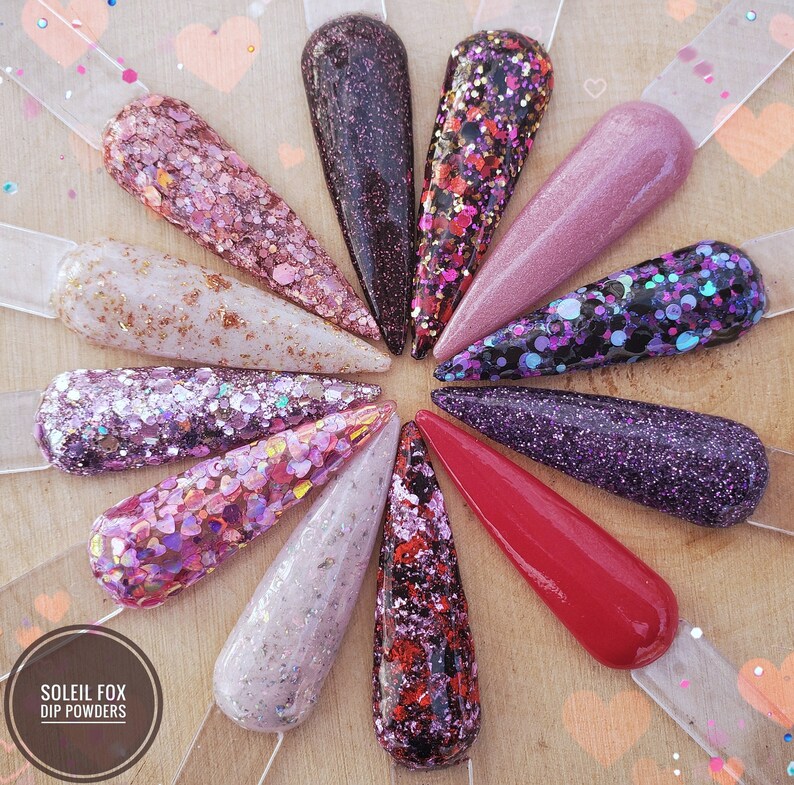 May include: A collection of nail dip powder samples in various colors and textures. The samples include glitter, shimmer, and solid colors, ranging from pinks and purples to reds and blacks. The Soleil Fox Dip Powders logo is visible.