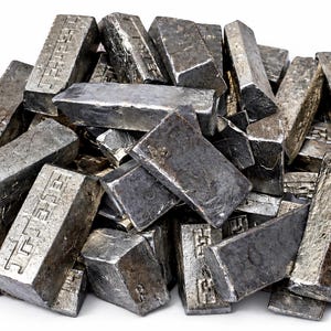 May include: A pile of rectangular metal ingots with a rough, textured, silver-gray finish. Each individual ingot features a stamped geometric pattern on its side, showing a series of interconnected square shapes. The metal pieces are stacked.