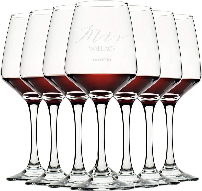A set of six elegant wine glasses with red wine, each glass custom-engraved with 'Mrs. Wallace' and a date '06.05.19', arranged in a row with a white background.