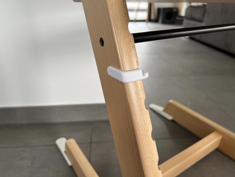 Puede incluir: Primer plano de una silla alta de madera con una correa de seguridad de pl&aacute;stico blanco. La silla tiene un acabado de madera clara y una serie de ranuras a lo largo del lado.
