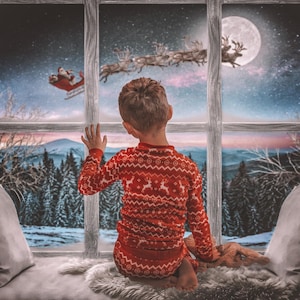 Op de afbeelding: Een kind in een rode pyjama met rendierenpatroon kijkt uit het raam naar de slee van de kerstman en rendieren die door een sterrenhemel vliegen. Een volle maan schijnt boven een besneeuwd bos.