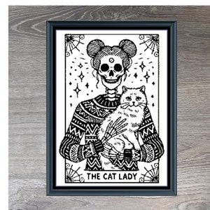 Könnte beinhalten: Gerahmter Schwarz-Weiß-Kunstdruck mit dem Titel "Cat Lady Monochrome". Das Kunstwerk zeigt eine Skelettfigur, die eine Katze hält, mit dem Text "The Cat Lady" unten. Die Maße sind 280 x 284.