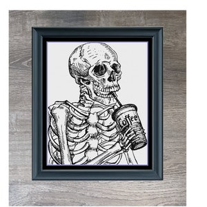 Op de afbeelding: Zwart-wit ingelijste kunstprint met een skelet dat koffie drinkt. Het kunstwerk, getiteld "Coffee Addiction", wordt gepresenteerd in een zwarte lijst tegen een grijze houten achtergrond.