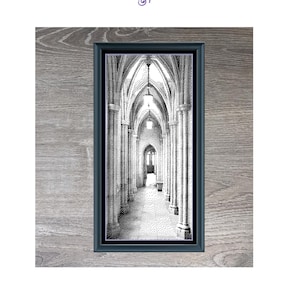 Op de afbeelding: Een ingelijste zwart-wit print getiteld "Cathedral Walkway". De afbeelding toont een lange gang met gewelfde plafonds en zuilen, die leidt naar een verre lichtbron. De lijst is donker en de print meet 21,4 x 46 cm.