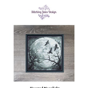 May include: A black and white cross-stitch pattern of a full moon with three crows flying in front of it. The moon is surrounded by bare branches. The pattern is framed in a dark wood frame. The text "Haunted Moonlight" and "120 X 120" is below the image.