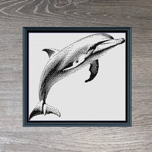 Może przedstawiać: Czarno-biała ilustracja punktowa skaczącego delfina, oprawiona w czarną ramę. Obraz zatytułowany "Dolphin Monochrome" ma wymiary 192 x 174 pikseli. U góry obrazu znajduje się tekst "Stitching Jules Design".