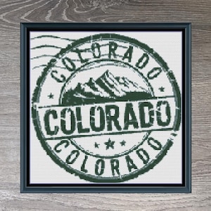 May include: A cross-stitch pattern of a green and white Colorado stamp with the text "COLORADO" in a circle. The pattern is 140 stitches wide by 140 stitches tall and uses 3 DMC colors.