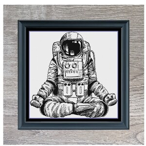 May include: Black and white illustration of an astronaut in a space suit sitting in a yoga pose. The image is framed in a gray wood frame. The text "Astronaut Yoga" is below the image.