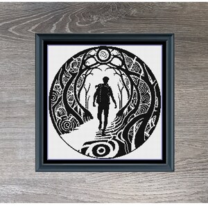 May include: Black framed artwork featuring a black and white cross-stitch design. The design depicts a person walking on a path through a stylized forest. The artwork is titled "Path Taken" and measures 210 x 210.