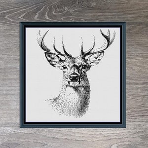 May include: Black and white cross-stitch pattern of a stag's head with antlers. The pattern is framed in a black frame and set against a woodgrain background. The text "The Stag" and "210 X 236" are below the image.