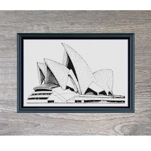 May include: A framed black and white cross-stitch depicting the Sydney Opera House. The artwork is titled "Sydney Opera House" and measures 34.0 cm x 21.0 cm. The background is a grey wood-effect. The image also includes the text "Stitching Jules Design".