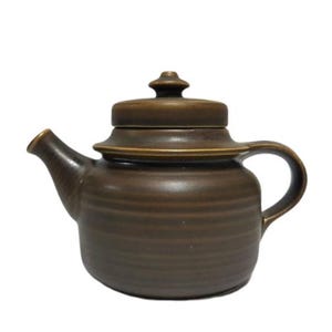 May include: A brown ceramic teapot with a lid. The teapot has a rounded body and a spout on the side. The teapot has a brown glaze with a subtle striped pattern.