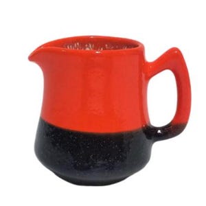May include: A red and black ceramic creamer with a rounded body and a handle. The creamer is glazed in a bright red colour on the top half and a black speckled glaze on the bottom half.