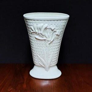 May include: A white ceramic vase with a textured surface and a raised floral design. The vase has a wide mouth and a rounded base.