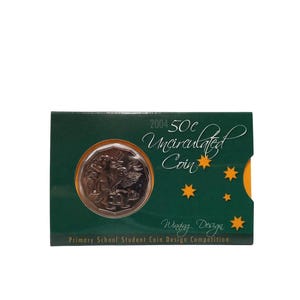 May include: A green and gold card containing a 2004 50c Uncirculated Coin. The coin features a design of a koala with wings. The card reads "Winning Design" and "Primary School Student Coin Design Competition".
