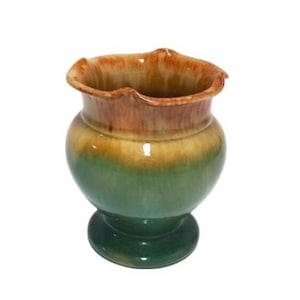 May include: A small, green and brown ceramic vase with a scalloped rim. The vase has a glazed finish and a rounded body.