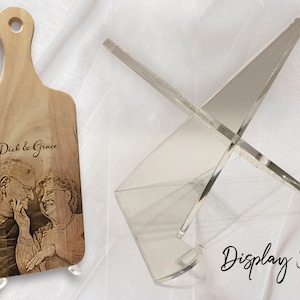 May include: A personalised wooden chopping board with a laser engraved photo of a couple and the text "Dick & Grace". The board is displayed on a clear acrylic stand.