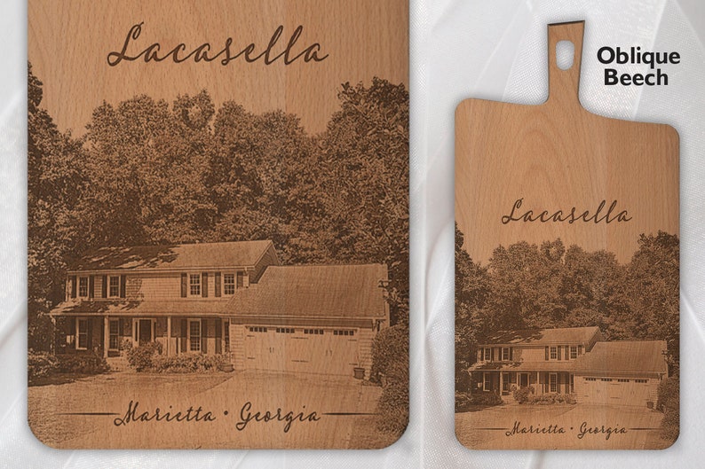 May include: A personalised wooden chopping board with a laser engraved image of a house and trees. The text "Lacasella" and "Marietta, Georgia" is engraved on the board. The board is made of oblique beech wood.