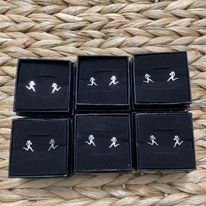 May include: Six black boxes with white running figure earrings inside. Each box contains two earrings.