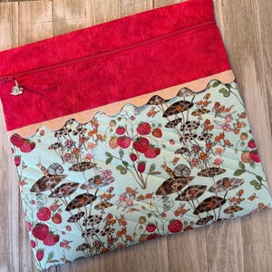 Pu&ograve; includere: Pochette con cerniera in tessuto trapuntato con parte superiore rossa e inferiore azzurra. Il tessuto inferiore presenta una stampa stravagante di fragole, lumache e funghi. Un bordo smerlato e una cerniera argentata completano il design.