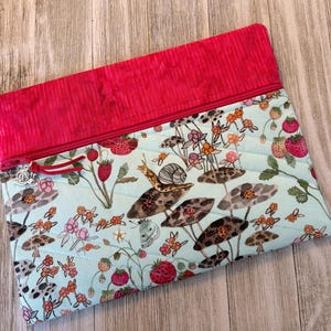 Pu&ograve; includere: Pochette in tessuto trapuntato con sfondo azzurro chiaro e fantasia di fragole e funghi. La parte superiore &egrave; rossa a tinta unita con chiusura a zip e un ciondolo decorativo. Ideale per trasportare piccoli oggetti.