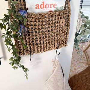 May include: A woven wall organiser with a magazine titled "adore home magazine" inside. The organiser has a wooden tag with a flamingo design. A towel hangs on a hook below the organiser.