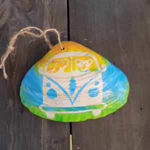 May include: A hand-painted seashell ornament featuring a tie-dye design in shades of blue, green, and yellow. The ornament depicts a white vintage van with two bears inside.