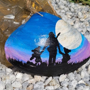 May include: A hand-painted seashell with a blue and purple sky, a white moon, and three black silhouettes of people walking in a line. The shell is a natural clam shell.